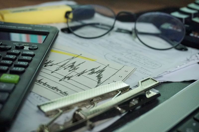 A calculator, reading glasses and printed financial charts on a desk