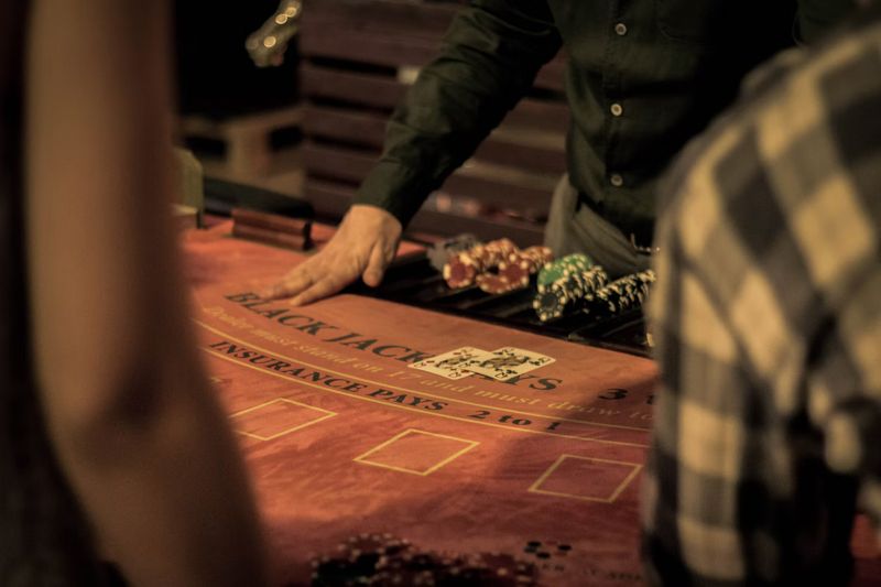 A dealer's hand on a blackjack table beside racks of chips